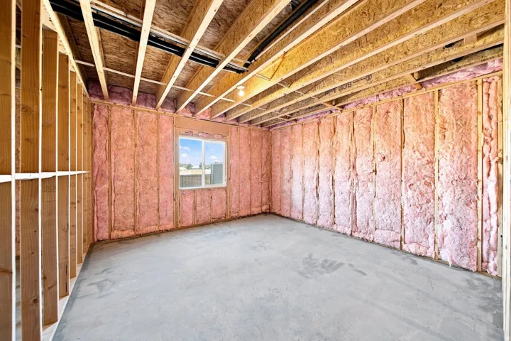 Unfinished basement space with exposed wood framing, ceiling joists, wall insulation, a concrete floor, and a single window