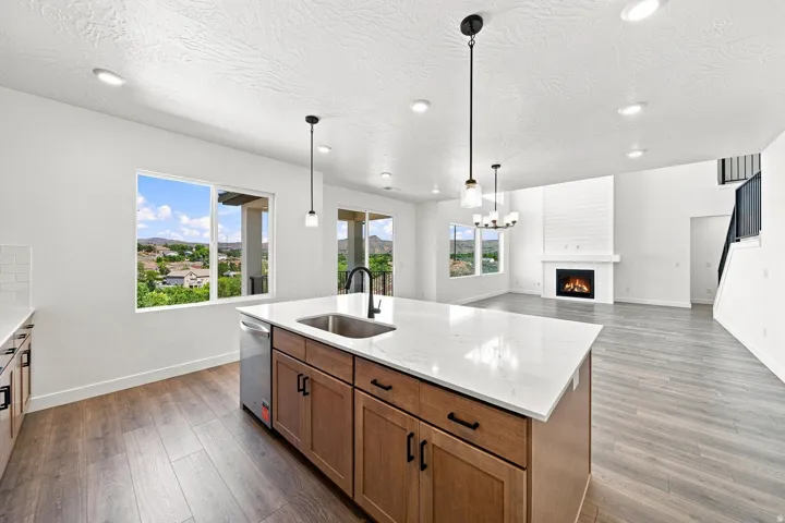 Expansive kitchen island with stone countertop and undermount sink, wood-finish flooring, white subway tile backsplash, and a contemporary fireplace with mantel