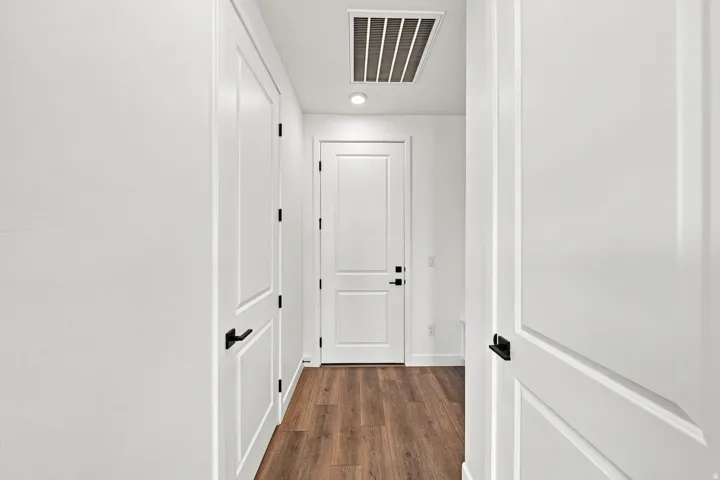 Bright hallway showcasing clean white panel doors with black hardware, warm wood-finish flooring, and recessed ceiling lighting throughout