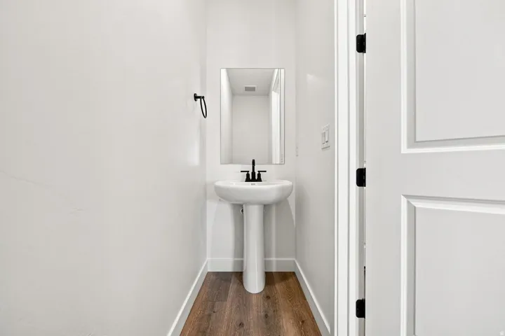 Pedestal sink with a matte black faucet, rectangular wall mirror, and wood-finish flooring