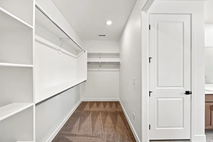 Walk-in closet featuring extensive built-in shelving, multiple hanging rods, recessed lighting, and patterned carpet flooring