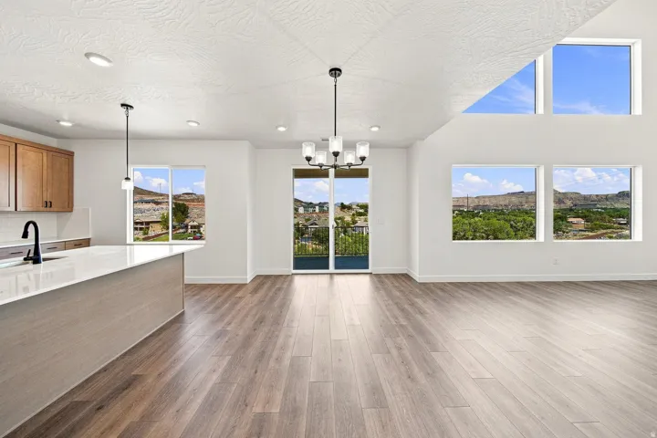 Vaulted ceilings with recessed lighting, wood-finish flooring, a kitchen island with a built-in sink, and multiple large windows