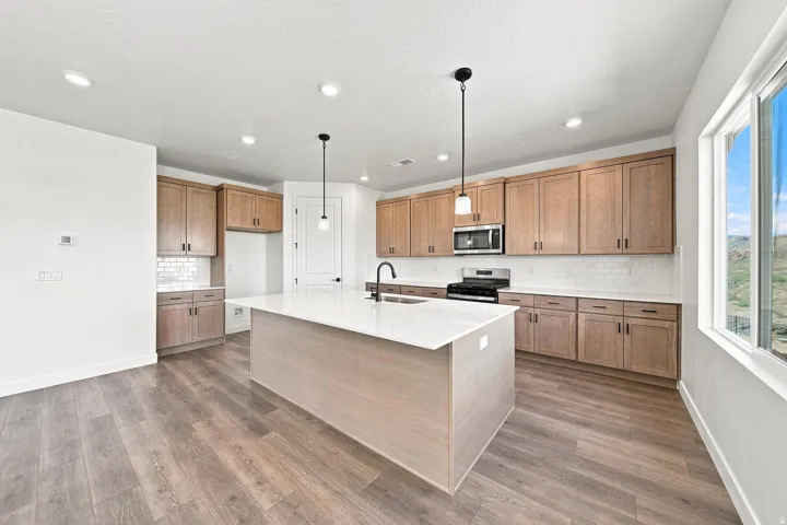 Kitchen featuring wood-finish flooring, recessed lighting, a central island with a white countertop, wood cabinetry, and a subway tile backsplash
