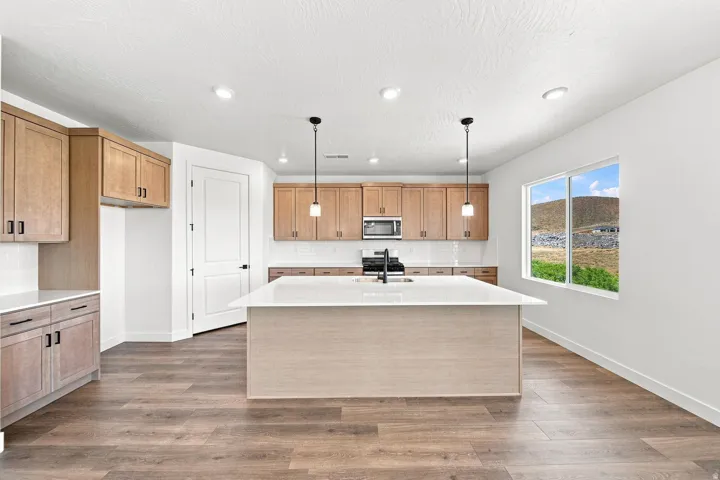 Kitchen featuring wood-finish flooring, light wood cabinetry, white countertops, a central island, and recessed lighting
