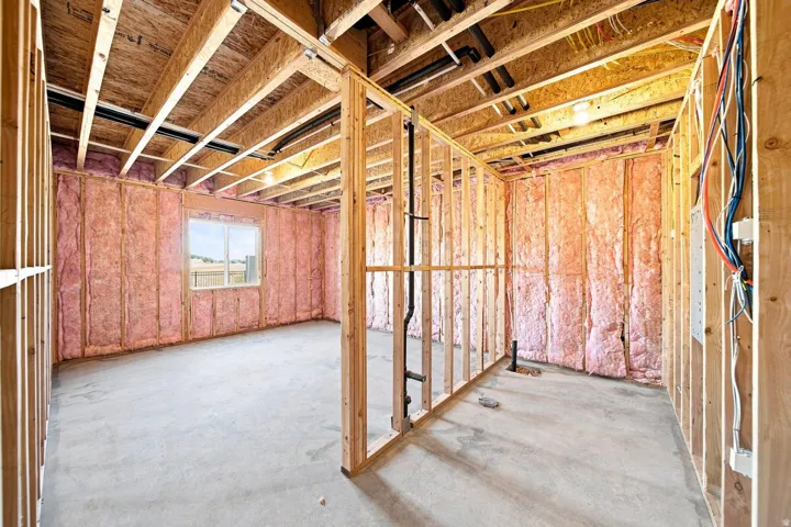 Unfinished basement featuring wood framing, exposed ceiling joists, insulation, concrete flooring, and a window