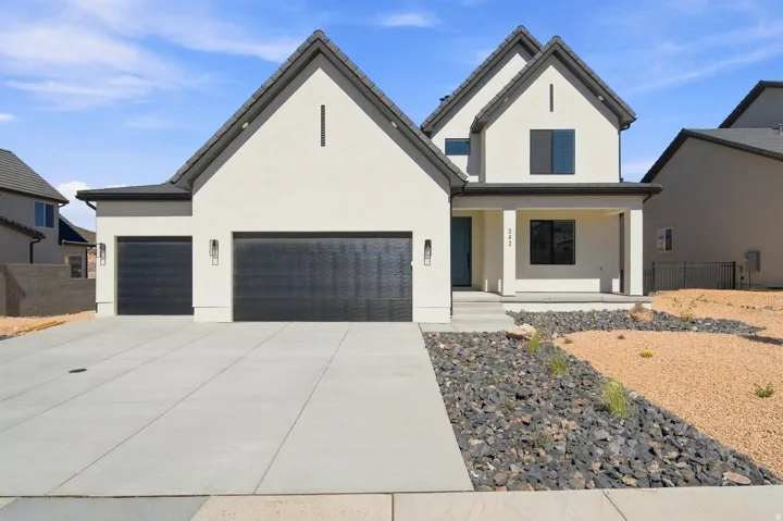 Contemporary stucco exterior with a covered entry, two-car garage, dark trim windows, and a low-maintenance landscape design