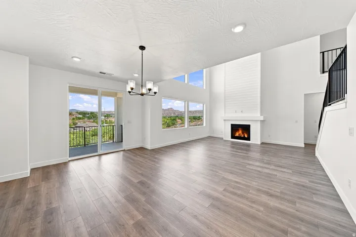 Spacious living area featuring wood-finish flooring, a contemporary chandelier, and a floor-to-ceiling fireplace with a white mantel