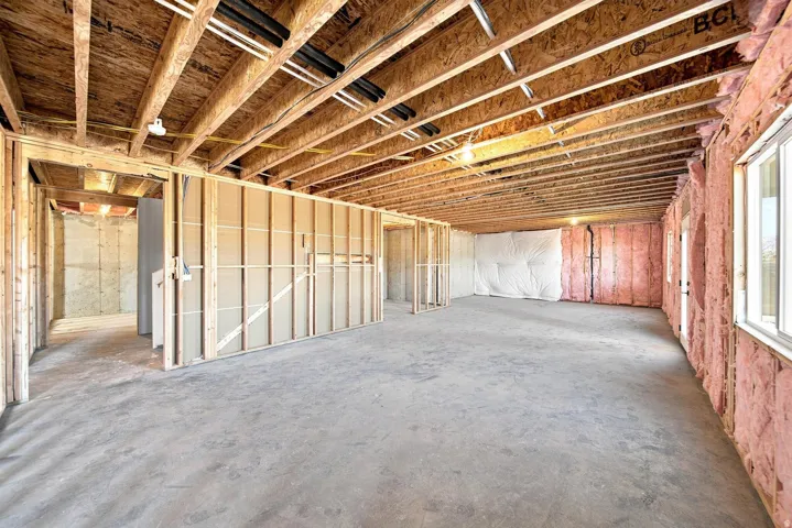Expansive unfinished basement featuring wood framing, exposed ceiling joists, concrete flooring, insulation, and multiple windows