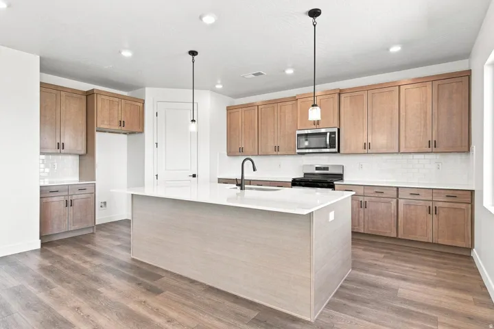 Kitchen featuring wood-finish cabinetry, white countertops, subway tile backsplash, and an island with pendant lighting
