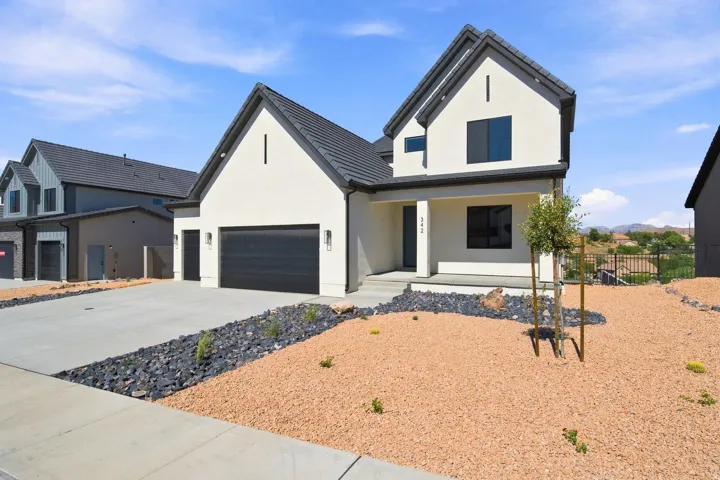 Modern stucco exterior with a dark tile roof, a two-car garage, a covered entry, and xeriscaped landscaping
