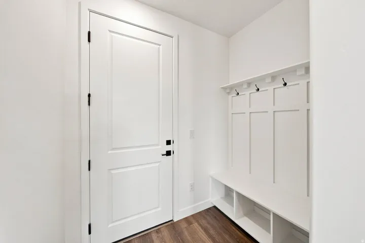 Built-in bench with integrated shelving and coat hooks, white paneled door with matte black hardware, and wood-finish flooring