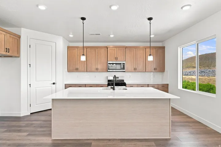 Kitchen features a large island with a light-toned base and a white countertop, wood-finish cabinetry, built-in microwave, and a white subway tile backsplash