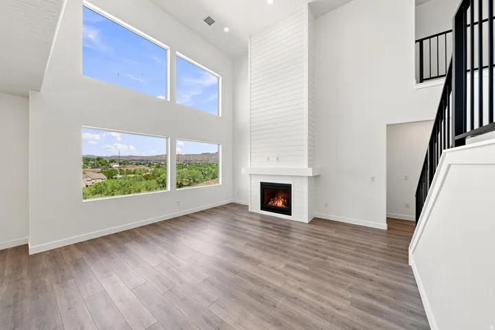 Expansive living area with soaring ceilings, multiple large windows, a shiplap-accented fireplace, and wood-finish flooring