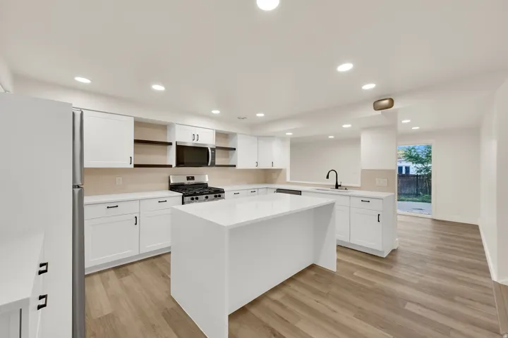 Modern kitchen featuring white cabinetry, a large center island, stainless steel appliances, and wood-finish flooring