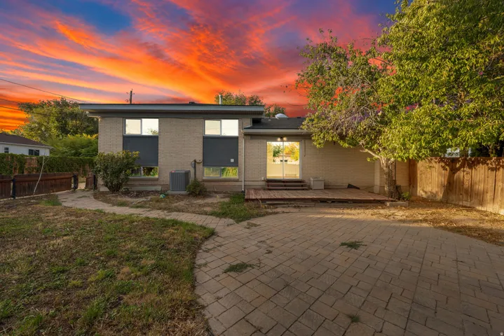 Rear exterior with a brick facade, private wood fencing, mature trees, a paver patio, and a wood deck