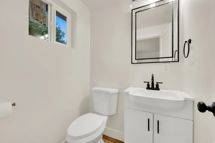 Bathroom featuring a white vanity with integrated sink, matte black faucet, framed mirror, white toilet, and window