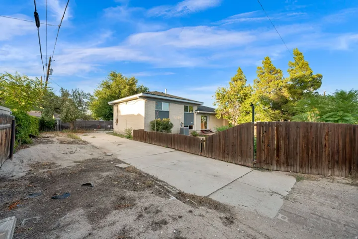 Concrete driveway with wood fencing, mature trees, and a stucco exterior