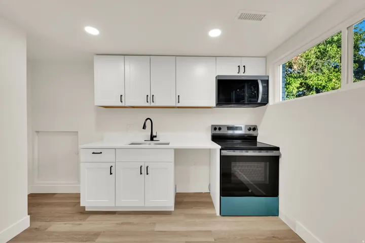 White cabinetry with black hardware, integrated microwave, stainless steel range, and wood-finish flooring
