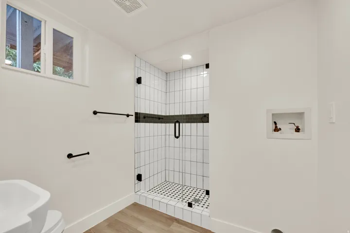 Glass-enclosed shower with vertical white subway tile and contrasting black accent band