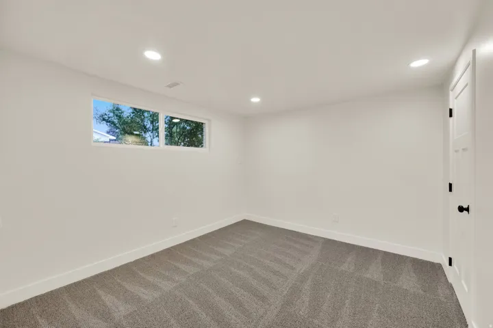 Recessed lighting, neutral wall tones, window with natural light, textured carpeting, and a paneled door with matte black hardware