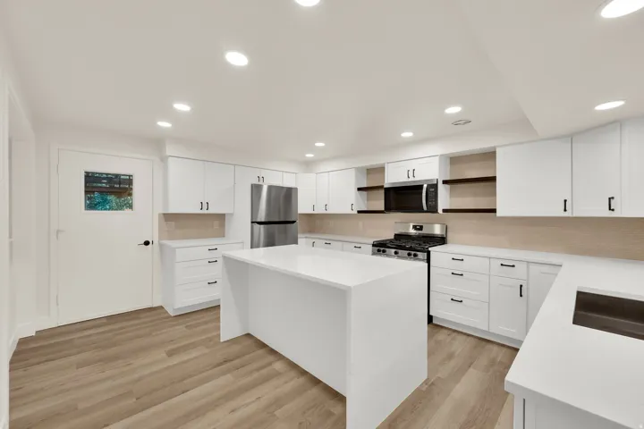 Modern kitchen featuring white cabinetry, a large center island, stainless steel appliances, and wood-finish flooring