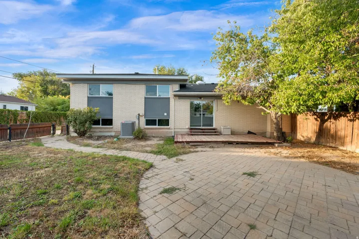 Brick exterior with multiple windows, sliding glass door, wood deck, paver patio, and mature trees