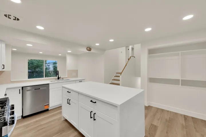 Modern kitchen featuring white cabinetry, a large center island with a solid surface countertop, stainless steel appliances, and wood-finish flooring