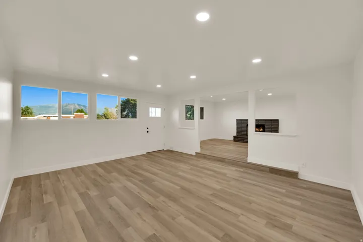 Expansive interior with wood-finish flooring, recessed lighting, multiple windows, a paneled door with frosted glass, and a brick fireplace in the background