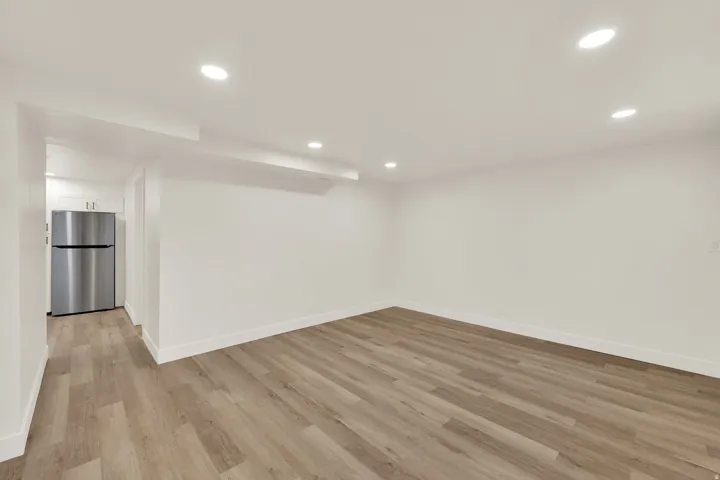 Recessed ceiling lighting, wood-finish flooring, white painted walls, and a stainless steel refrigerator