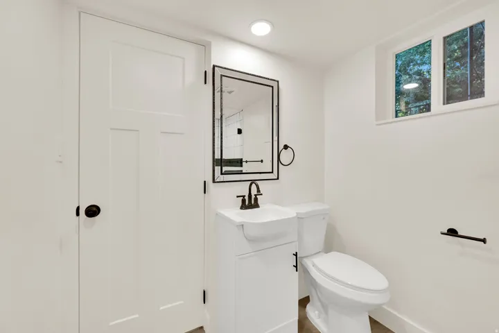White panel door with black hardware, white vanity with black faucet, framed mirror, and recessed lighting