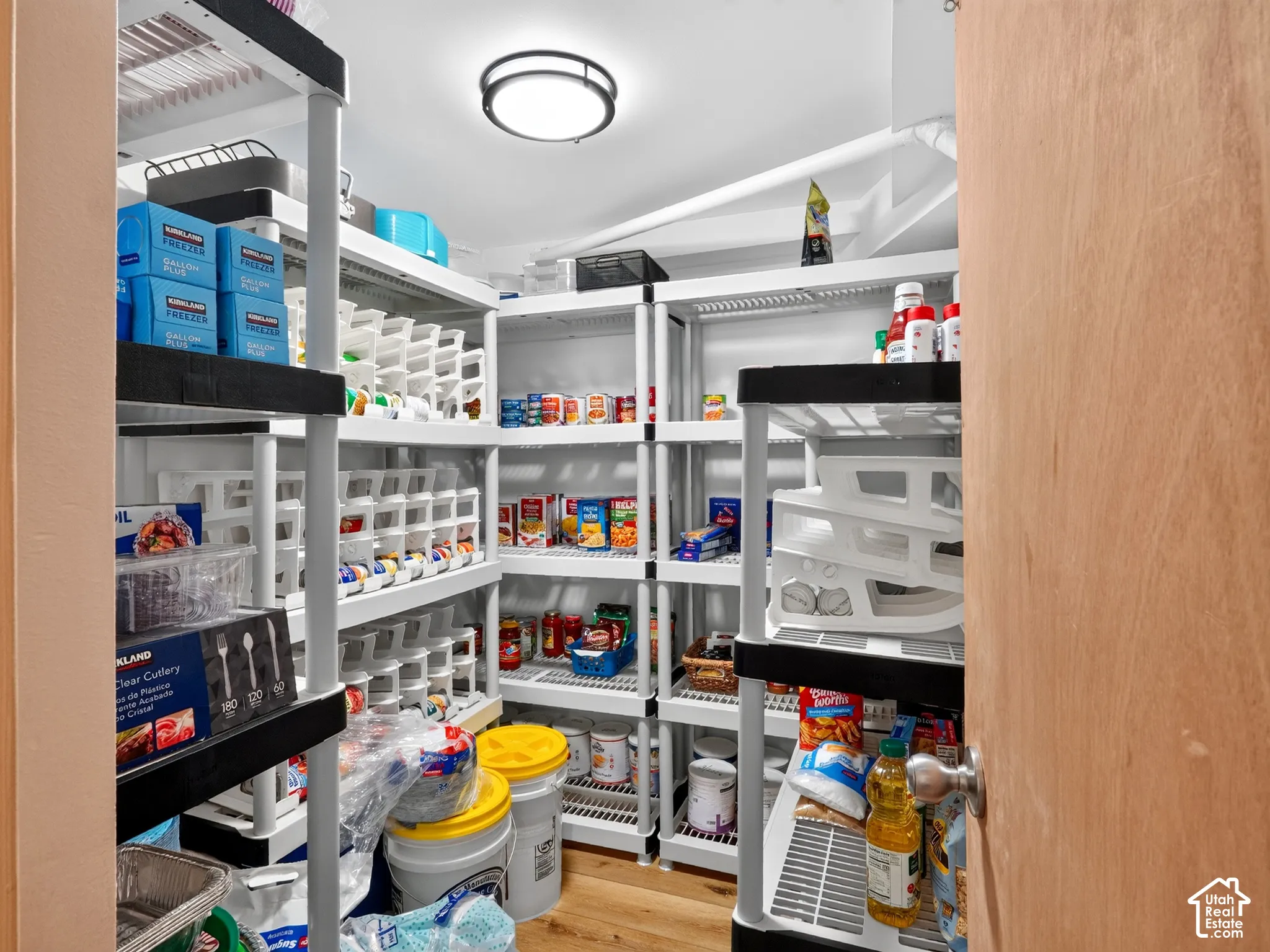 Dedicated pantry space featuring extensive shelving, wood-finish flooring, and overhead lighting