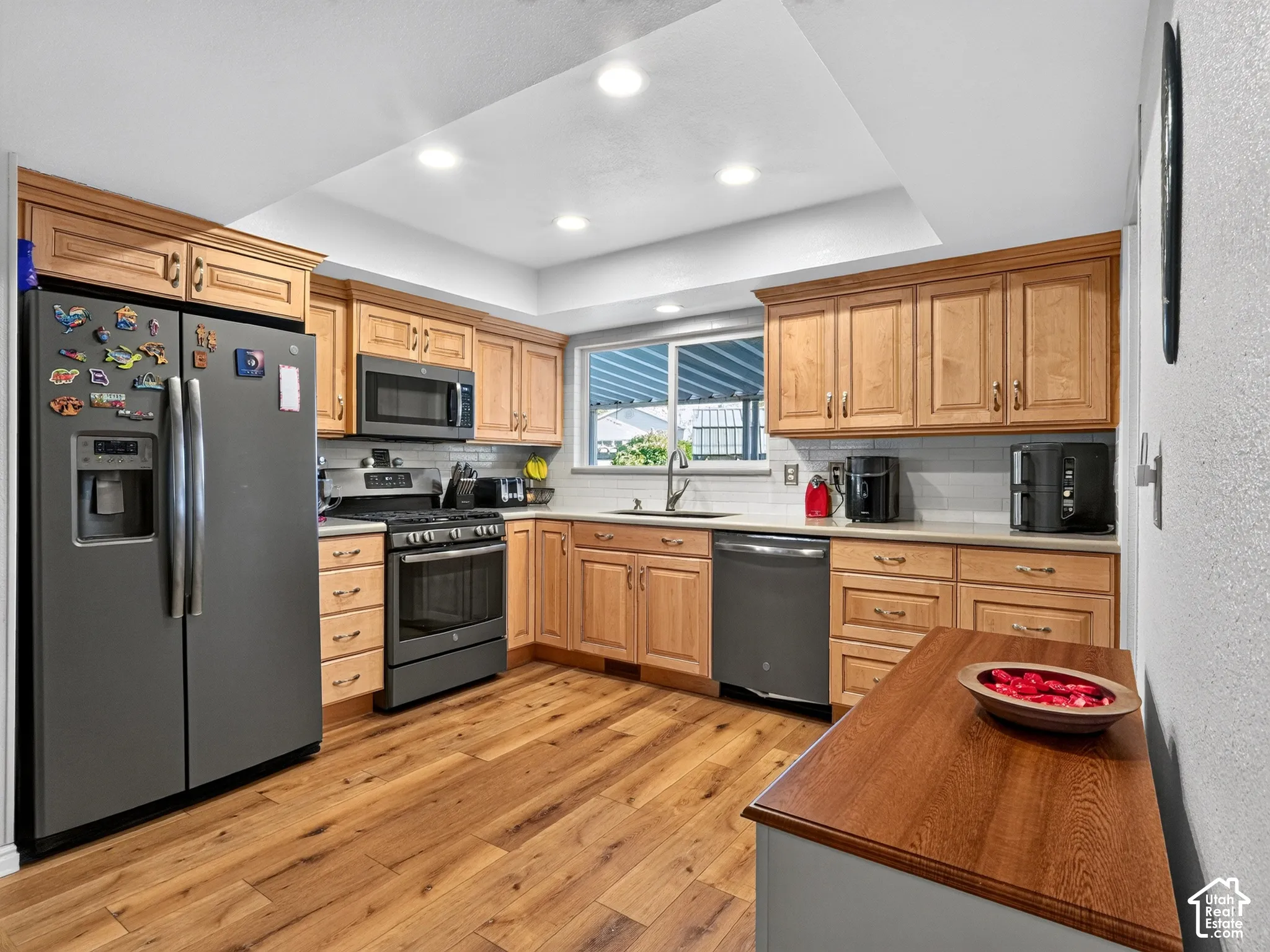 Wood-finish flooring, recessed lighting, wood cabinetry, stainless steel appliances, and a tile backsplash