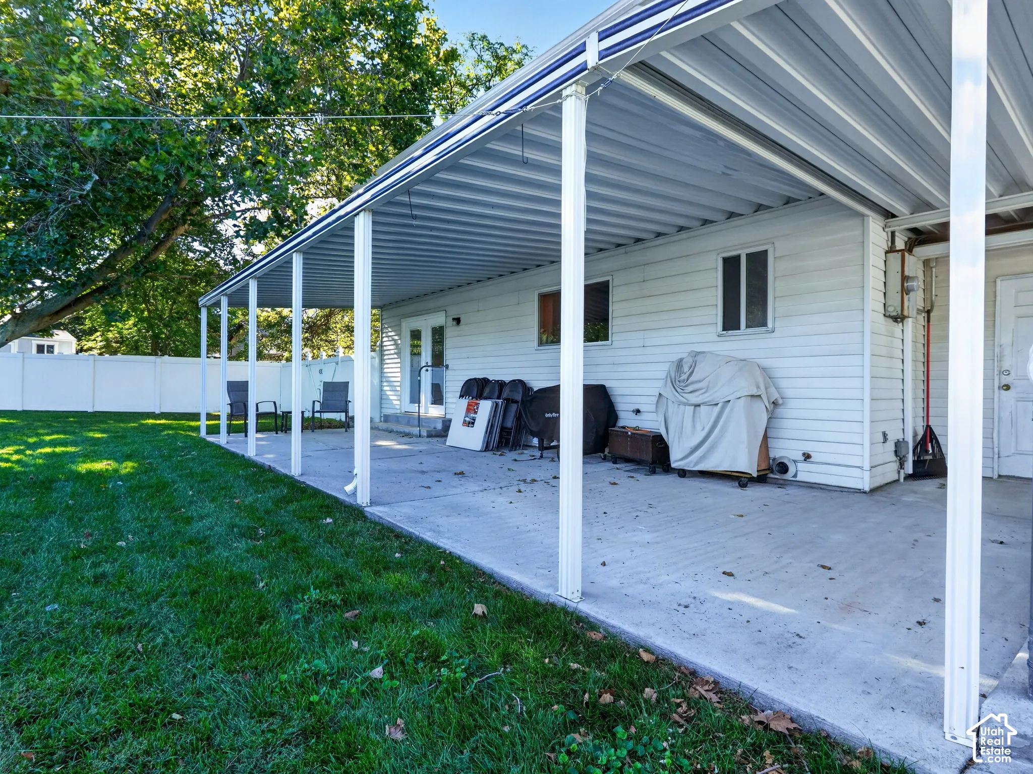 Expansive concrete patio with a full-length covered awning, siding exterior, and a fenced perimeter