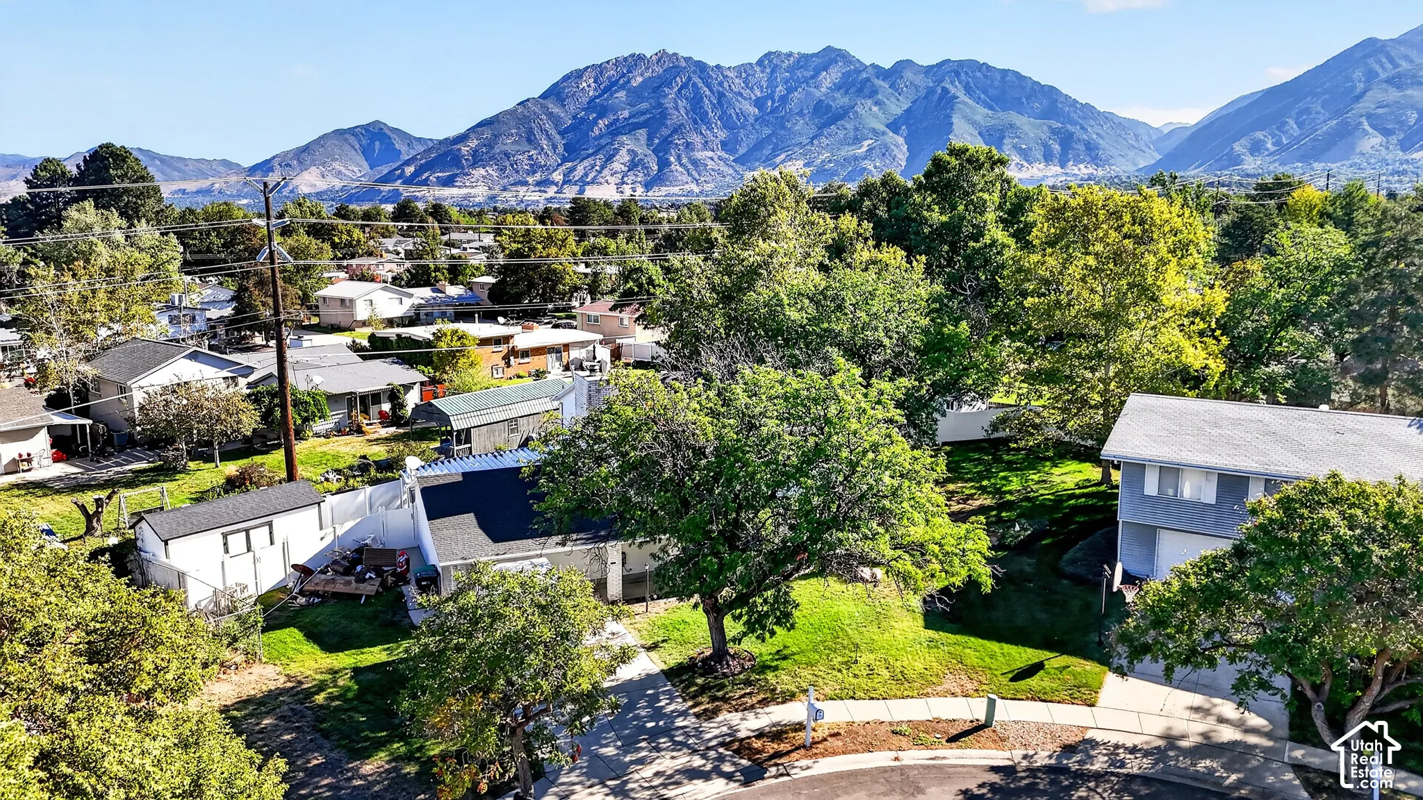 Mature trees and manicured lawns frame residential properties, with a prominent mountain range in the background