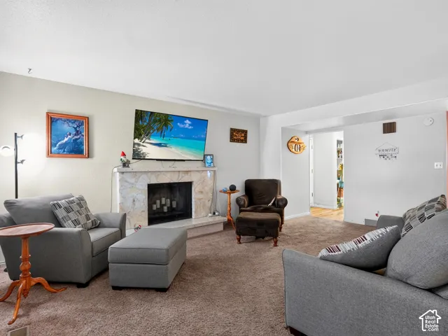 Carpeted living area featuring a stone-clad fireplace with hearth and a recessed firebox