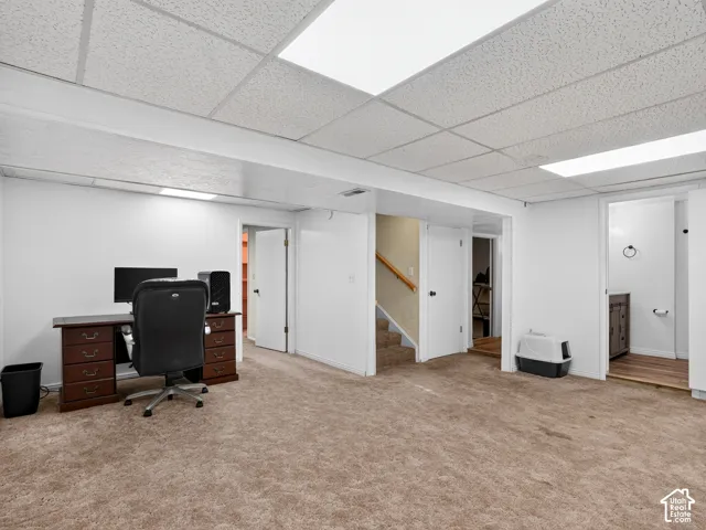 Carpeted flooring, drop ceiling with integrated lighting, white walls, and wood-finish handrail on staircase