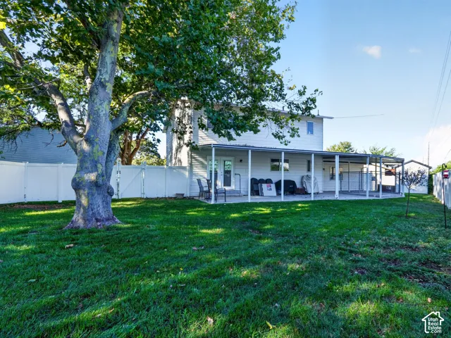 Expansive lawn with mature trees, fenced perimeter, and a covered patio area