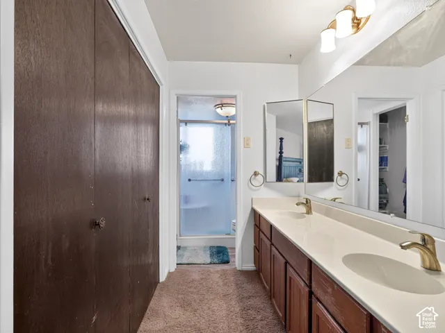 Double vanity with dual undermount sinks, wood-finish cabinetry, a full-width mirror, and a glass-enclosed shower
