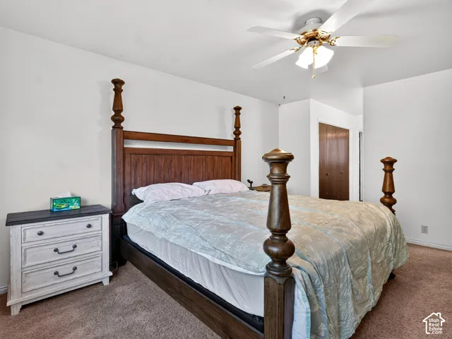Plush carpeted flooring, white painted walls, and a ceiling fan with integrated lighting