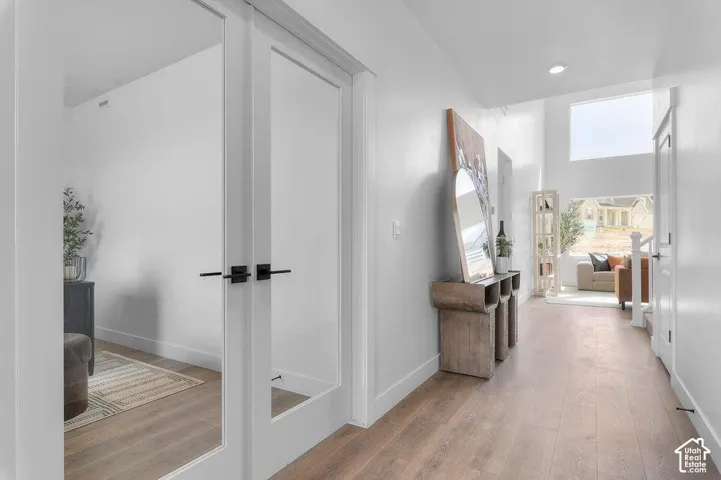 White walls, wood-finish flooring, glass-paneled doors with black hardware, and high ceilings with transom windows
