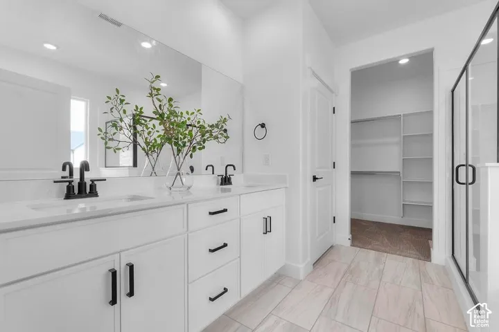 Dual vanity with undermount sinks, extended countertop, black fixtures, and a walk-in closet with built-in shelving