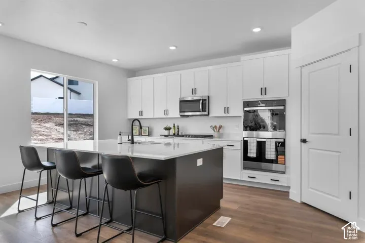 Kitchen featuring white cabinetry, a center island with countertop seating, built-in double ovens, stainless steel appliances, and wood-finish flooring