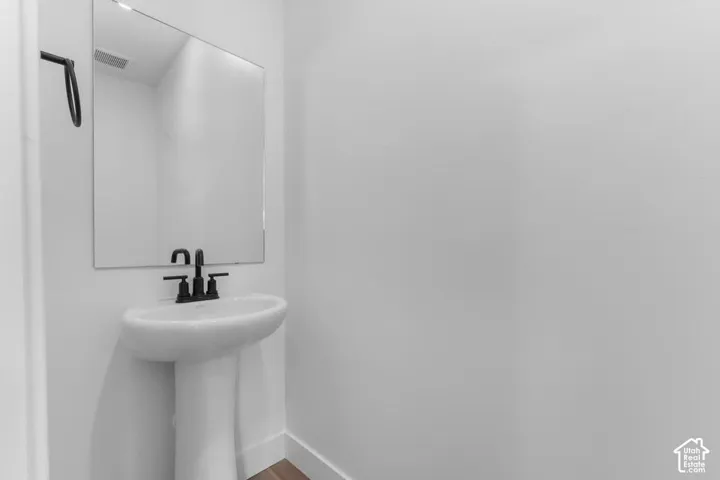 Pedestal sink with a matte black faucet, wall-mounted mirror, and wood-finish flooring