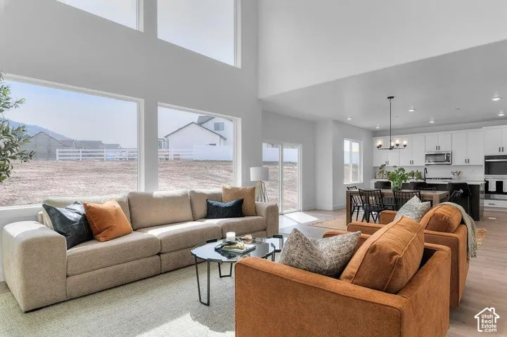 Open-concept living space with high ceilings, expansive windows, wood-finish flooring, a modern kitchen with white cabinetry, and recessed lighting