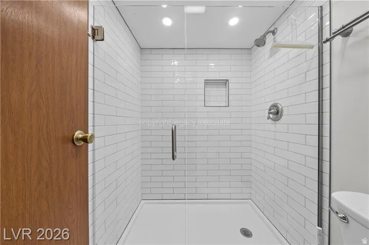 Frameless glass shower enclosure with white subway tile, built-in shower niche, and a brushed nickel shower head