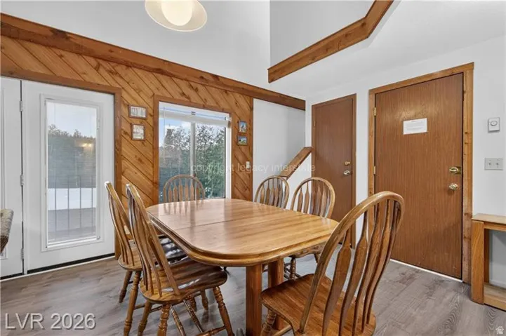 Wood-finish flooring, wood-paneled accent wall, natural light from exterior door, and high ceiling with exposed wood beams