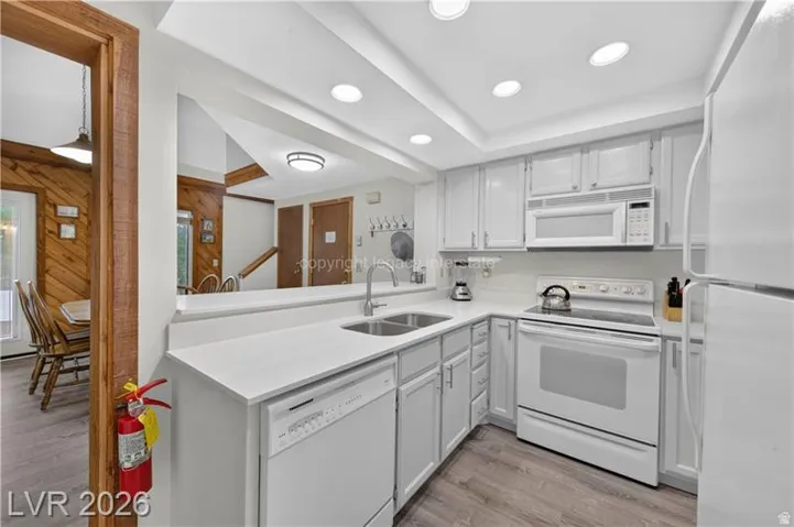 Kitchen featuring white cabinetry, white appliances, light-toned countertops, and wood-finish flooring