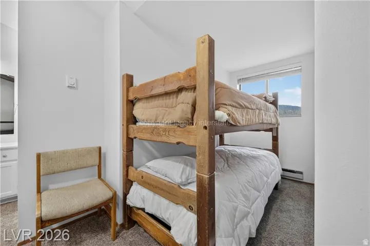 Carpeted room featuring a wooden bunk bed, white walls, and a window with outdoor scenery