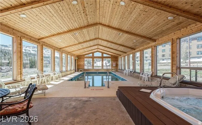 Indoor swimming pool with an adjacent hot tub, set within a wood-paneled room featuring a vaulted ceiling and expansive windows