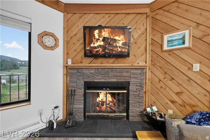 Stone-clad fireplace with slate hearth, diagonal wood-paneled accent wall, and expansive window with mountain scenery